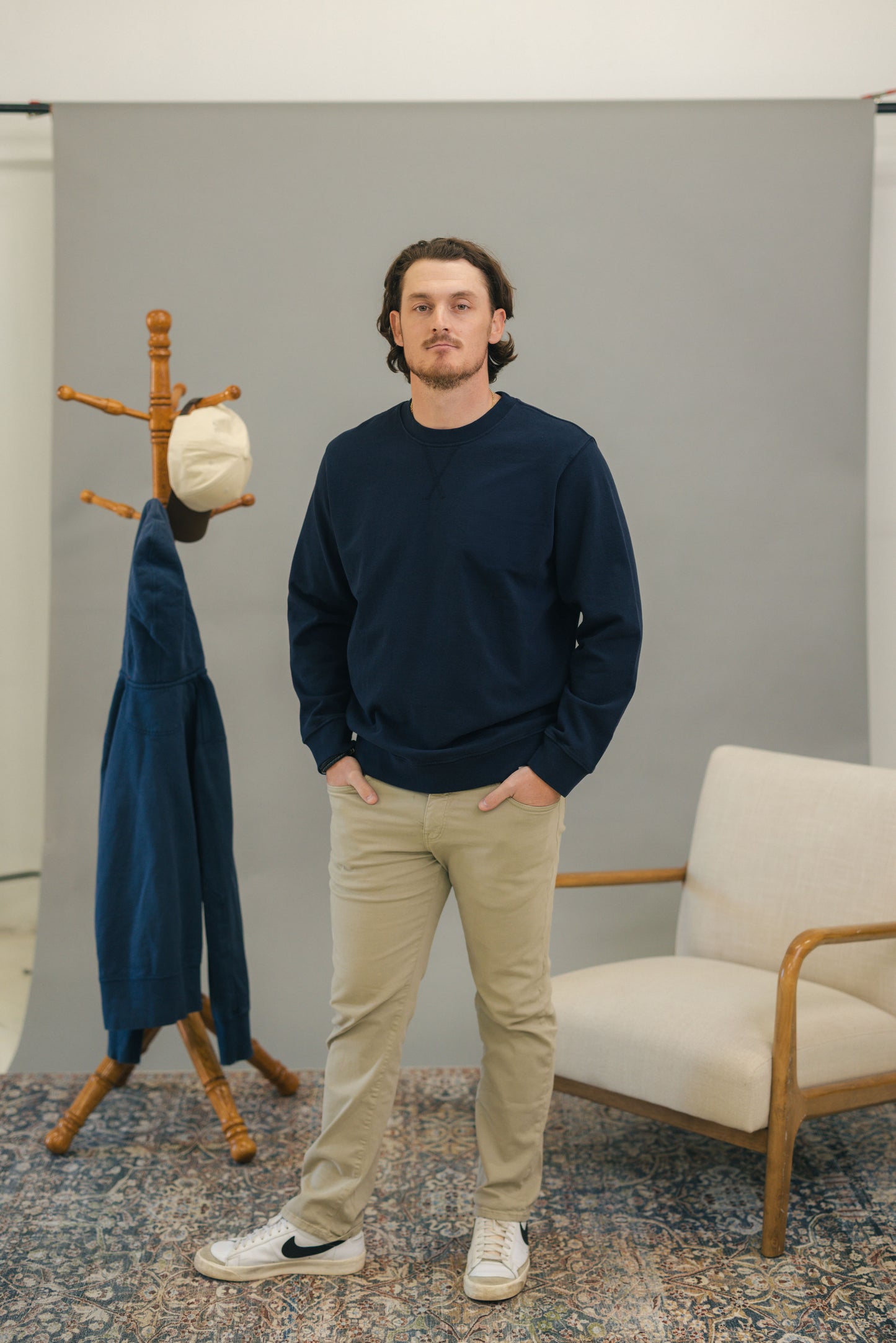 Man standing with navy crewneck sweatshirt with carpet, chair, coatrack