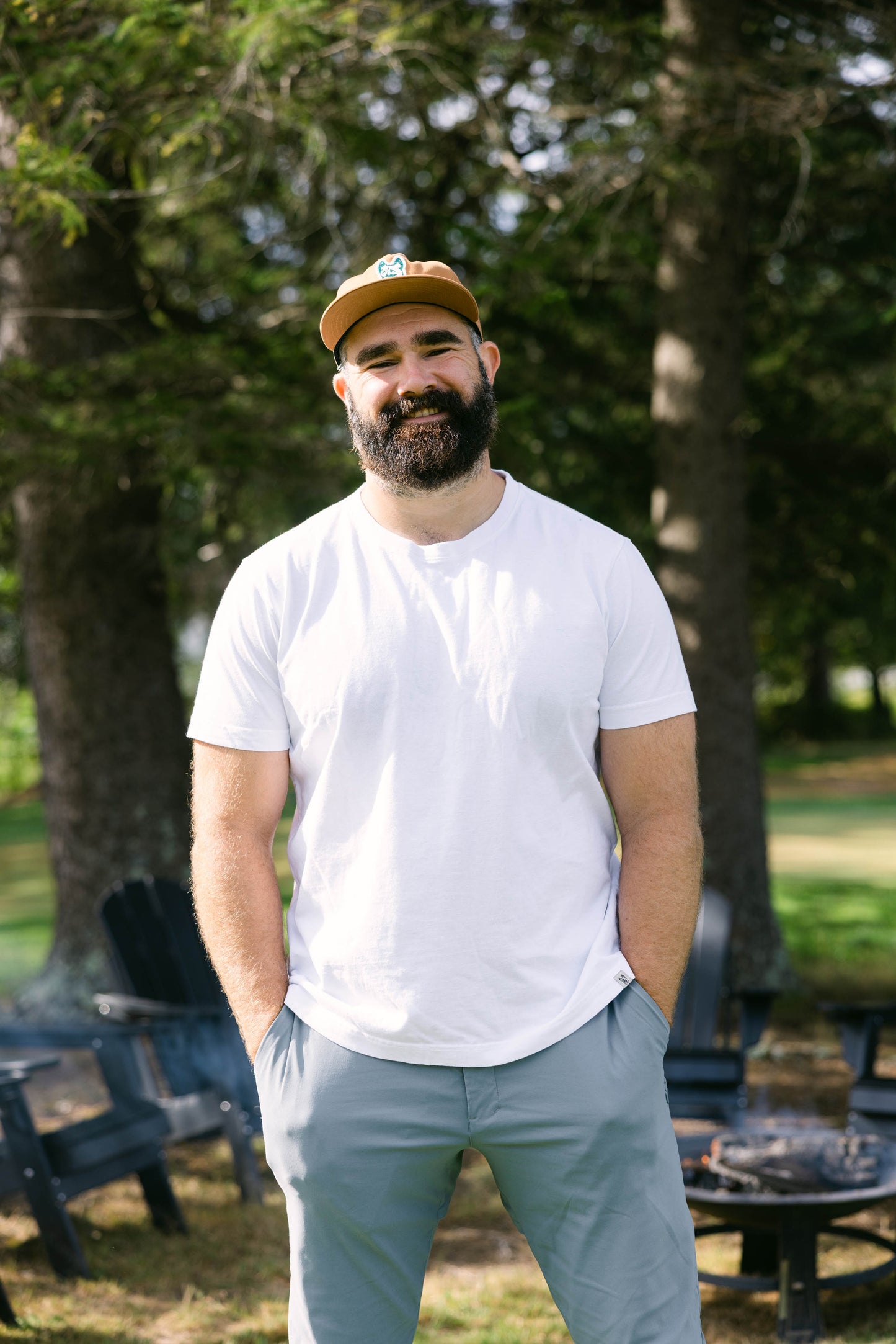 Man wearing a white t-shirt and beige cap standing outdoors with trees in the background