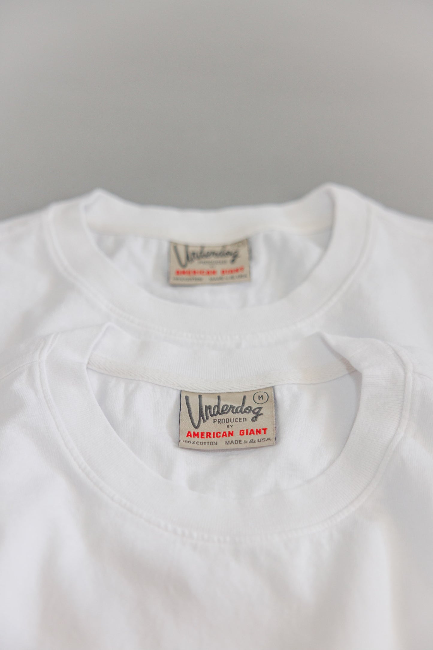 Close up of two white shirts with woven labels at back neck