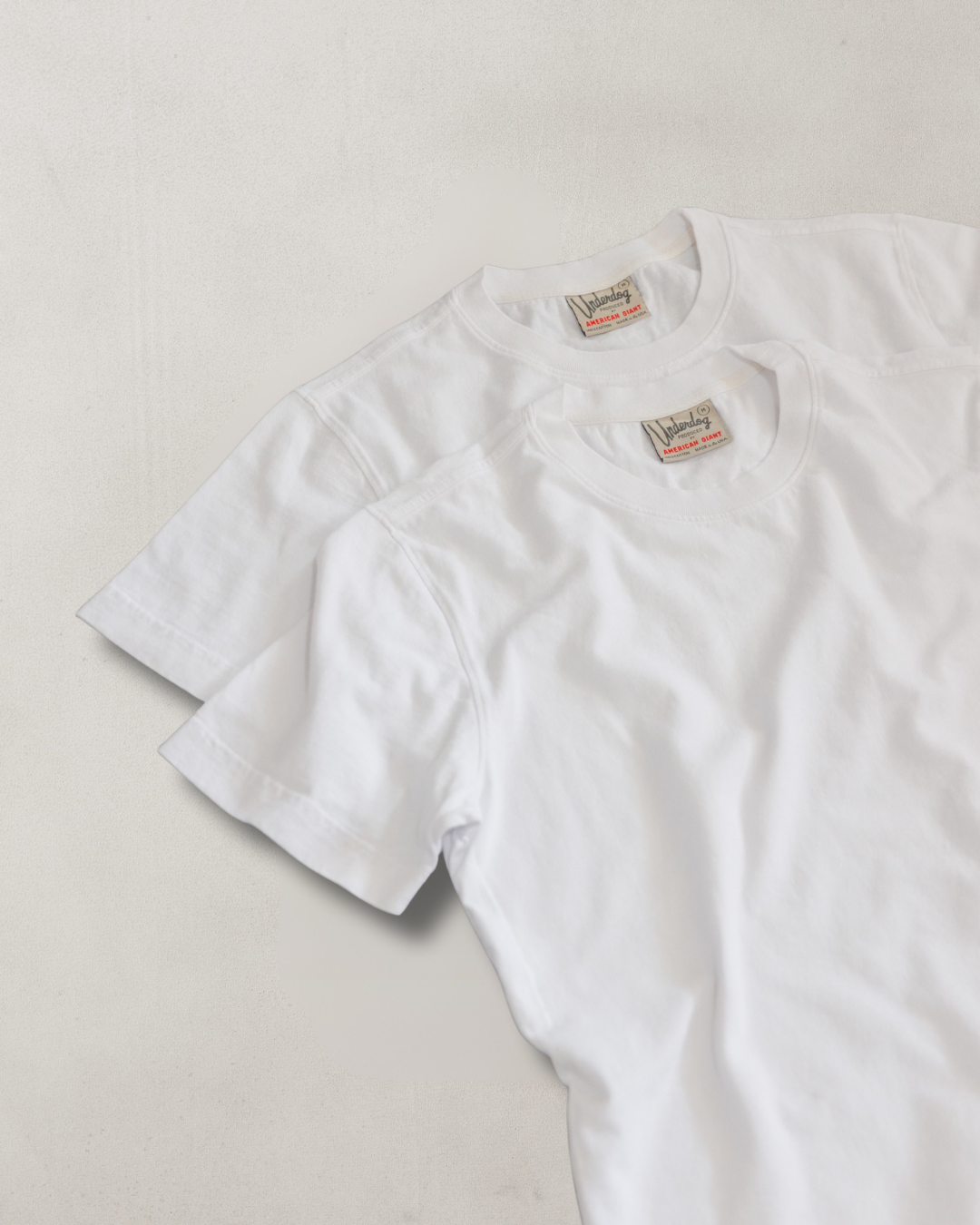 Two white t-shirts with labels on a light gray background
