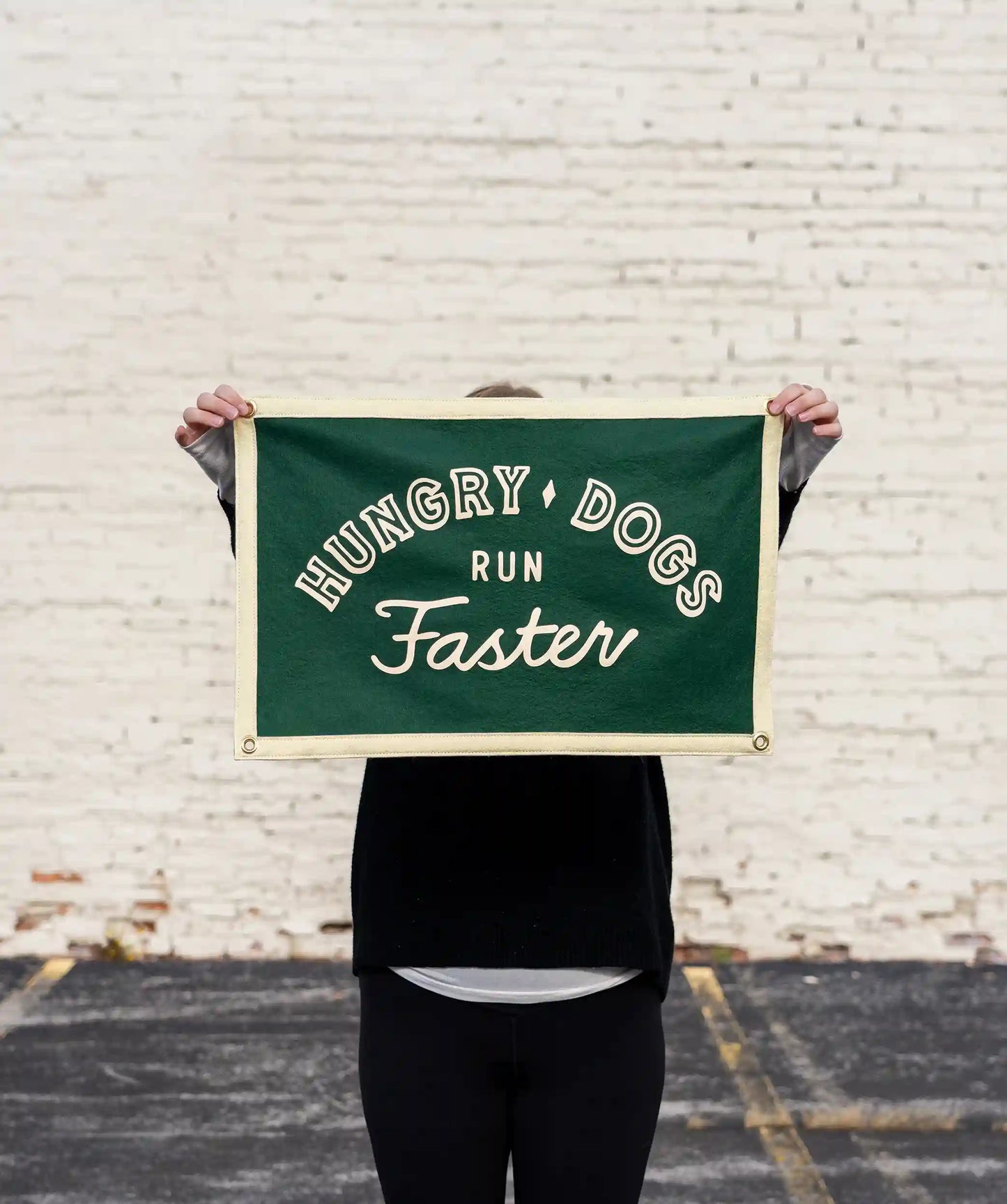 Person holding a green banner with cream-colored edges, featuring the text 'Hungry Dogs Run Faster' in bold and script fonts