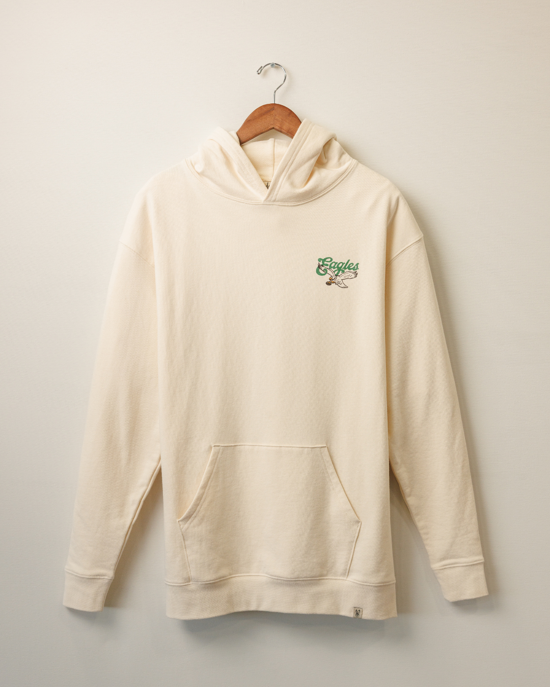 Beige hoodie with a logo on a hanger against a light background