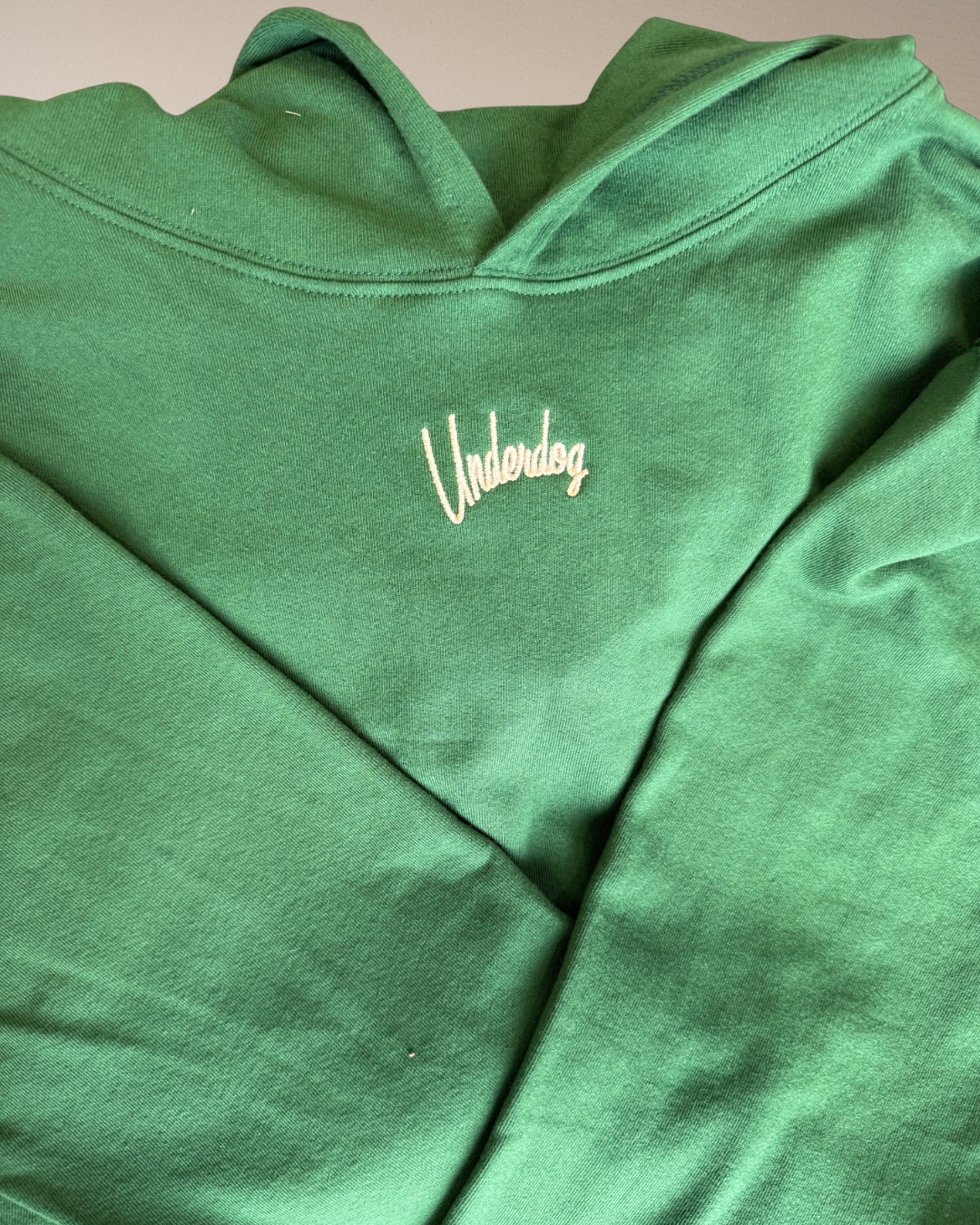 Green hoodie with 'Underdog' logo on a beige background
