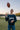 Man in navy blue crewneck Underdog sweatshirt tossing football in the air on the river bank