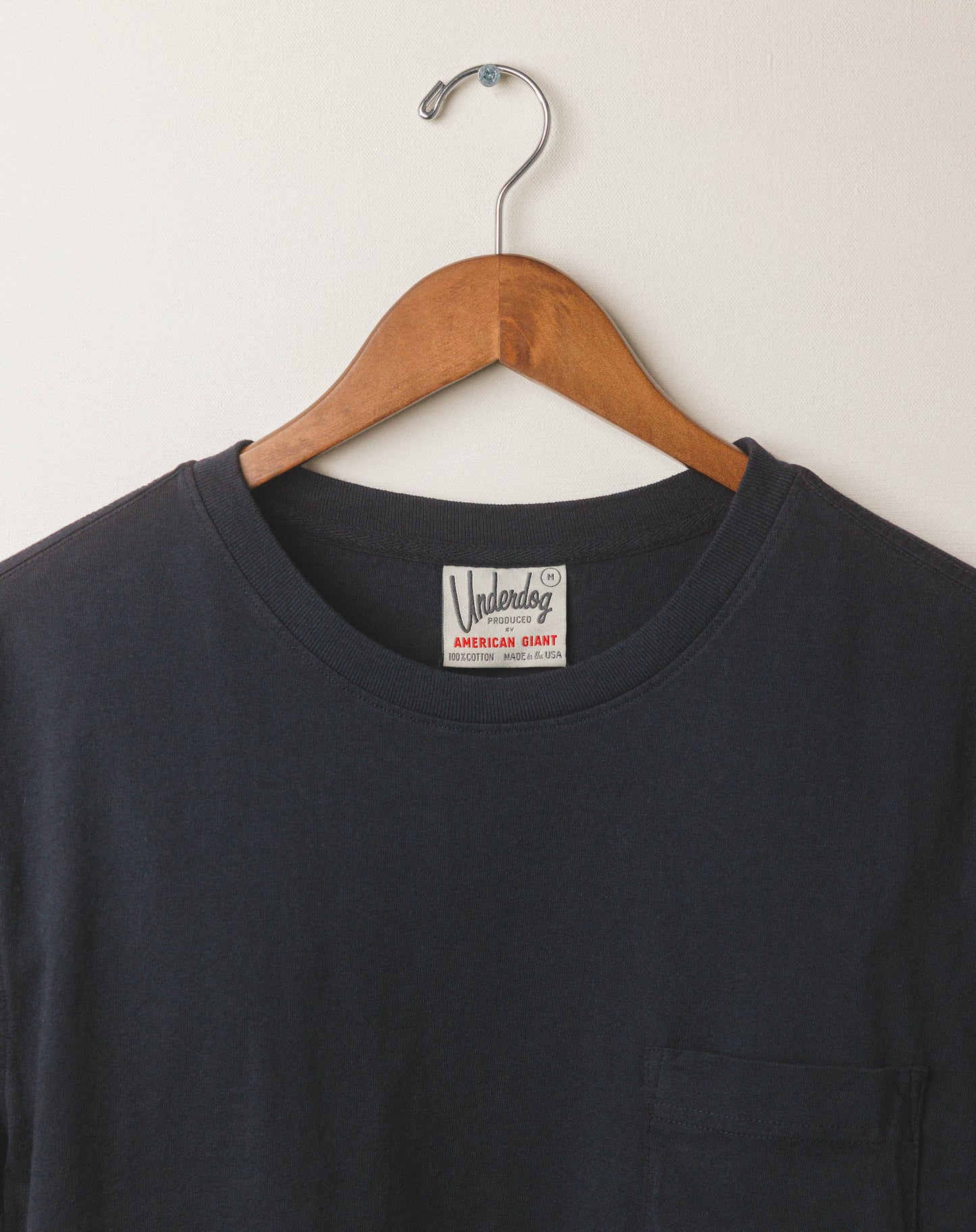 Black t-shirt with a brand label on a wooden hanger against a white background
