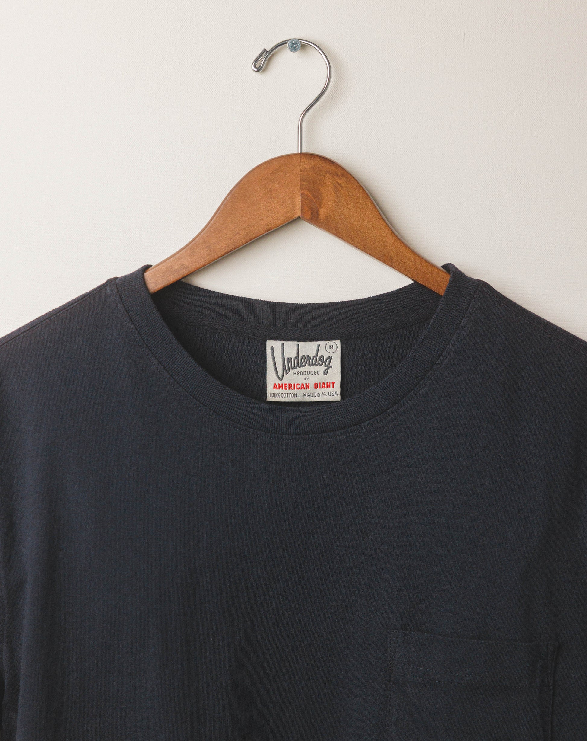 Black t-shirt with a brand label on a wooden hanger against a white background