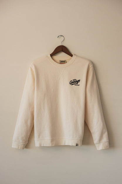Beige sweatshirt with a logo on a hanger against a beige wall