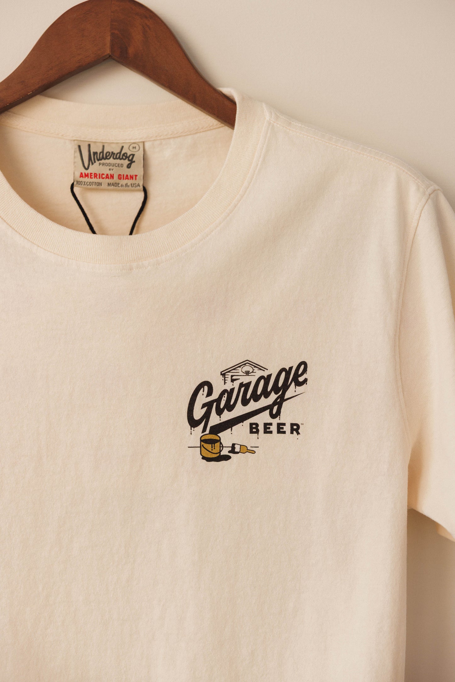 Beige t-shirt with 'Garage Beer' logo on a wooden hanger