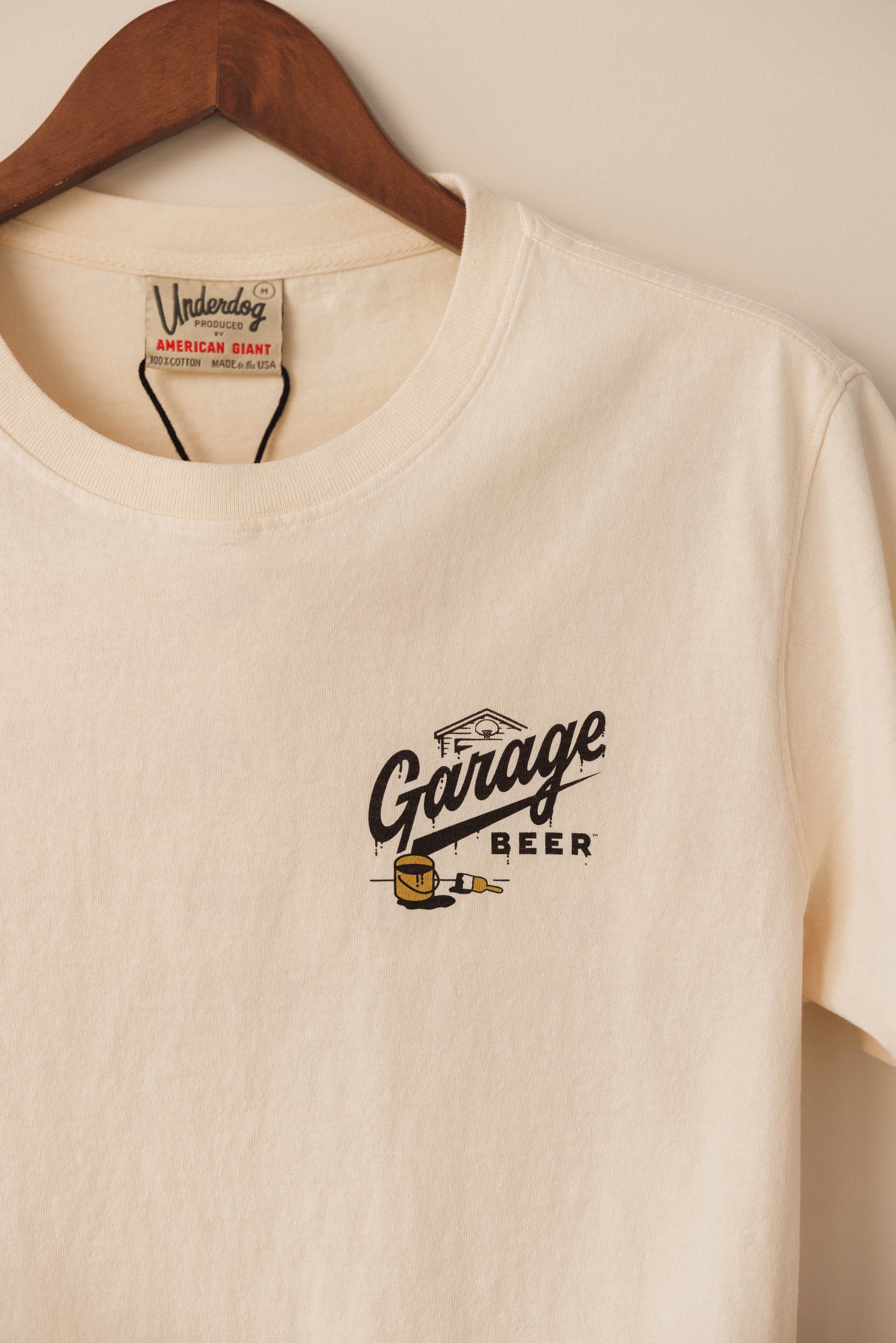 Beige t-shirt with 'Garage Beer' logo on a wooden hanger
