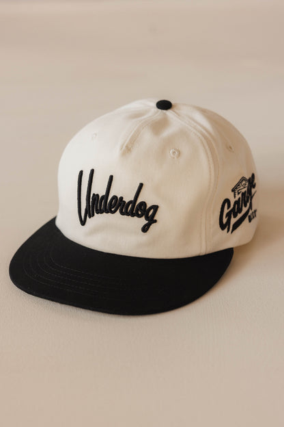 White and black cap with 'Underdog' and 'The Going' text on a beige background