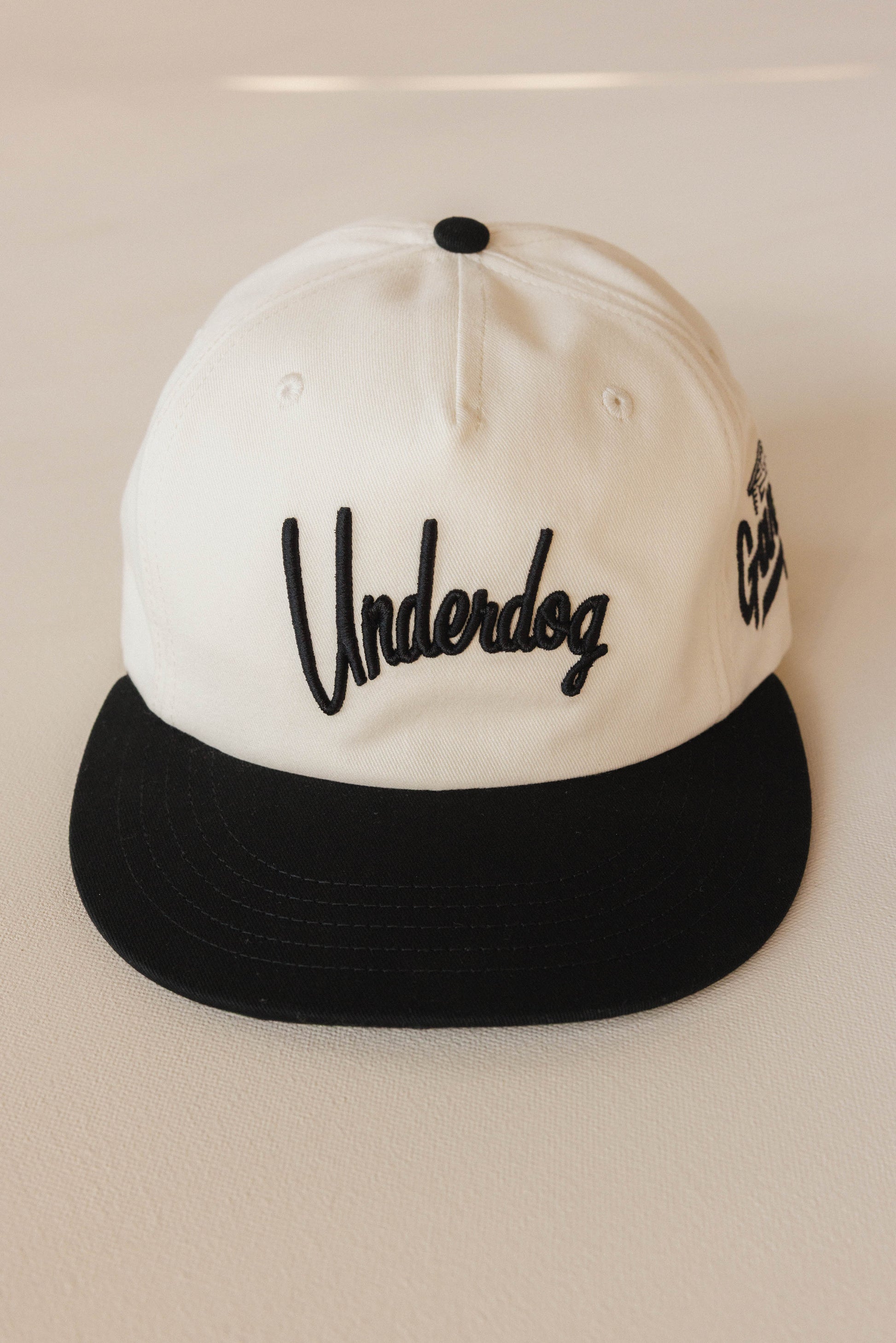 White and black cap with 'Underdog' logo on a light background