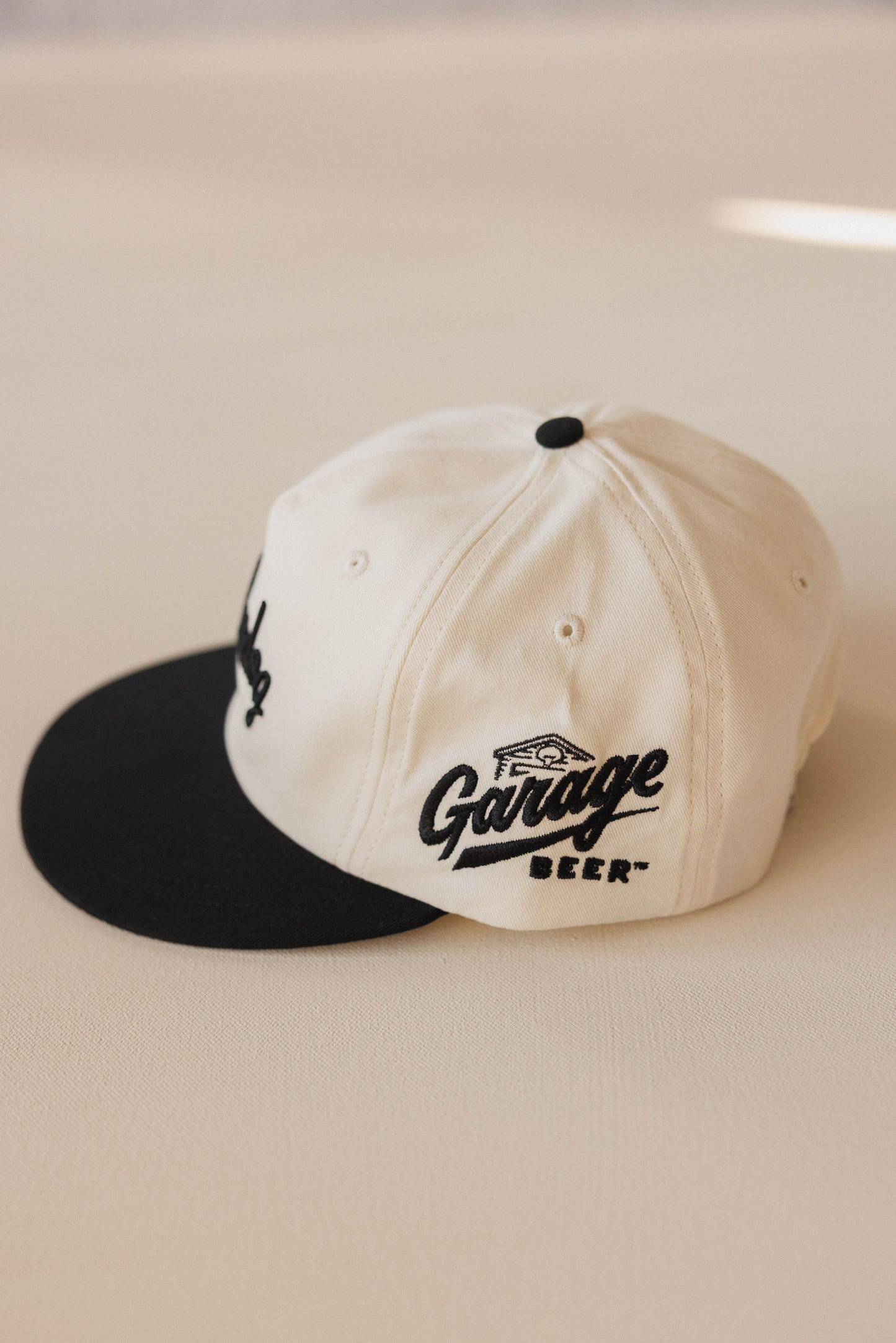 Two-tone cap with black visor and white主体, featuring 'Garage Beer' branding on a beige background.