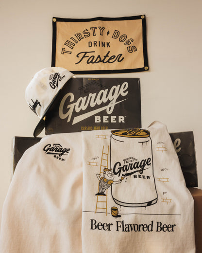 Garage Beer branded items including a hat, towel, and banner on a wall.
