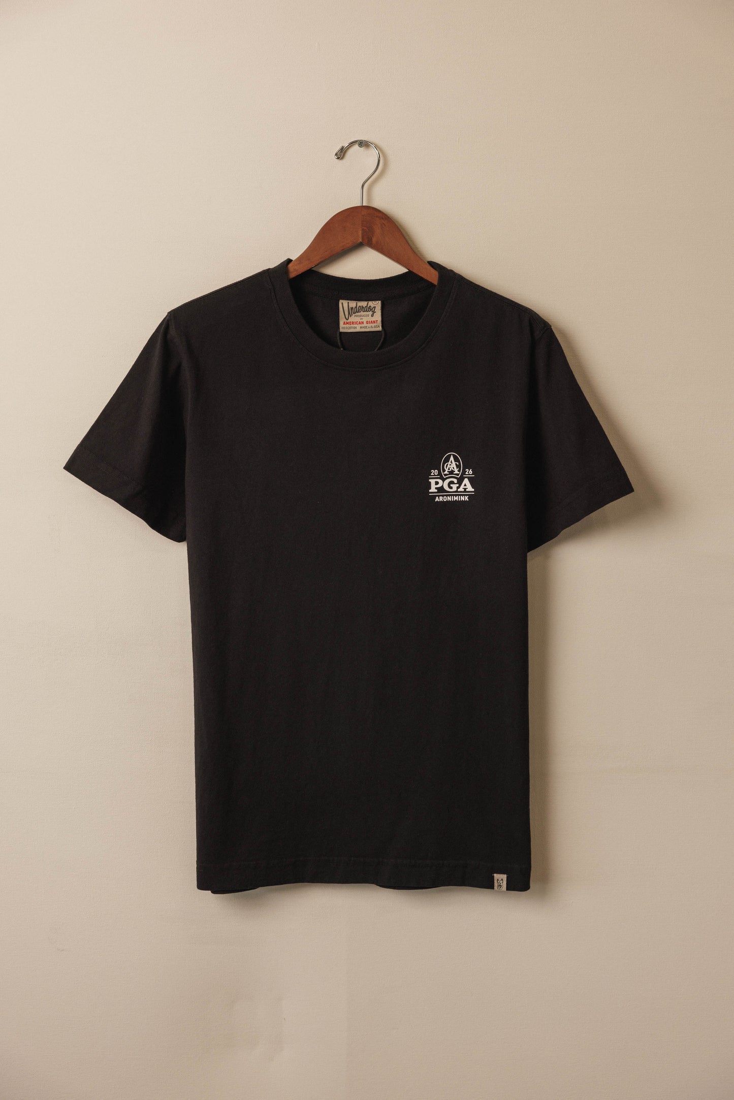 Black t-shirt with a logo on a hanger against a beige wall