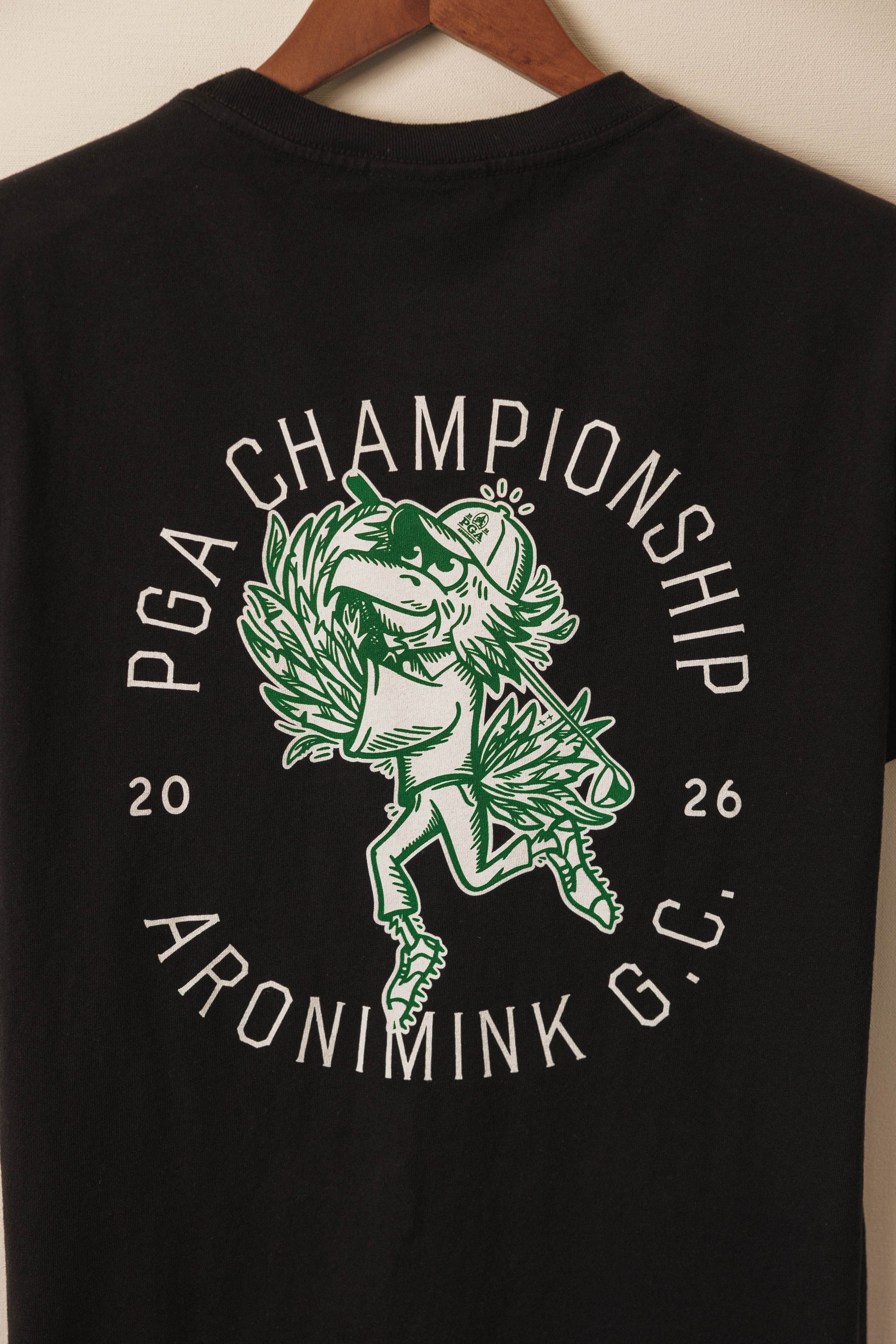 Black t-shirt with green and white graphic design on a wooden hanger