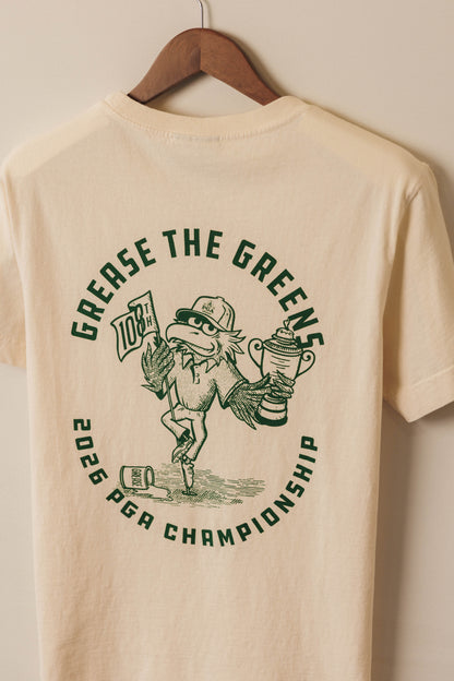 Beige t-shirt with green graphic and text on a hanger against a beige wall