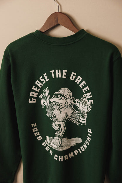 Green sweatshirt with graphic design and text on a hanger against a beige wall
