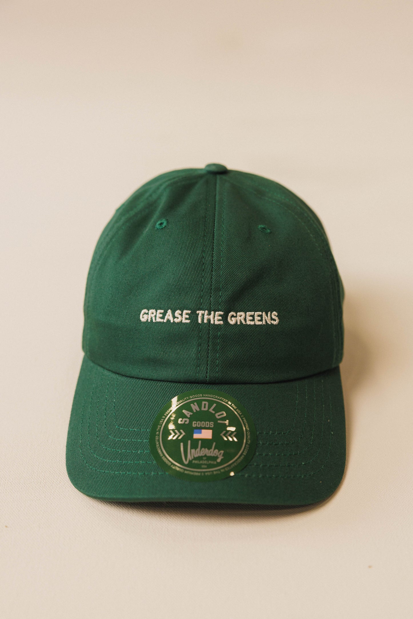Green cap with 'Grease the Greens' text on a beige background
