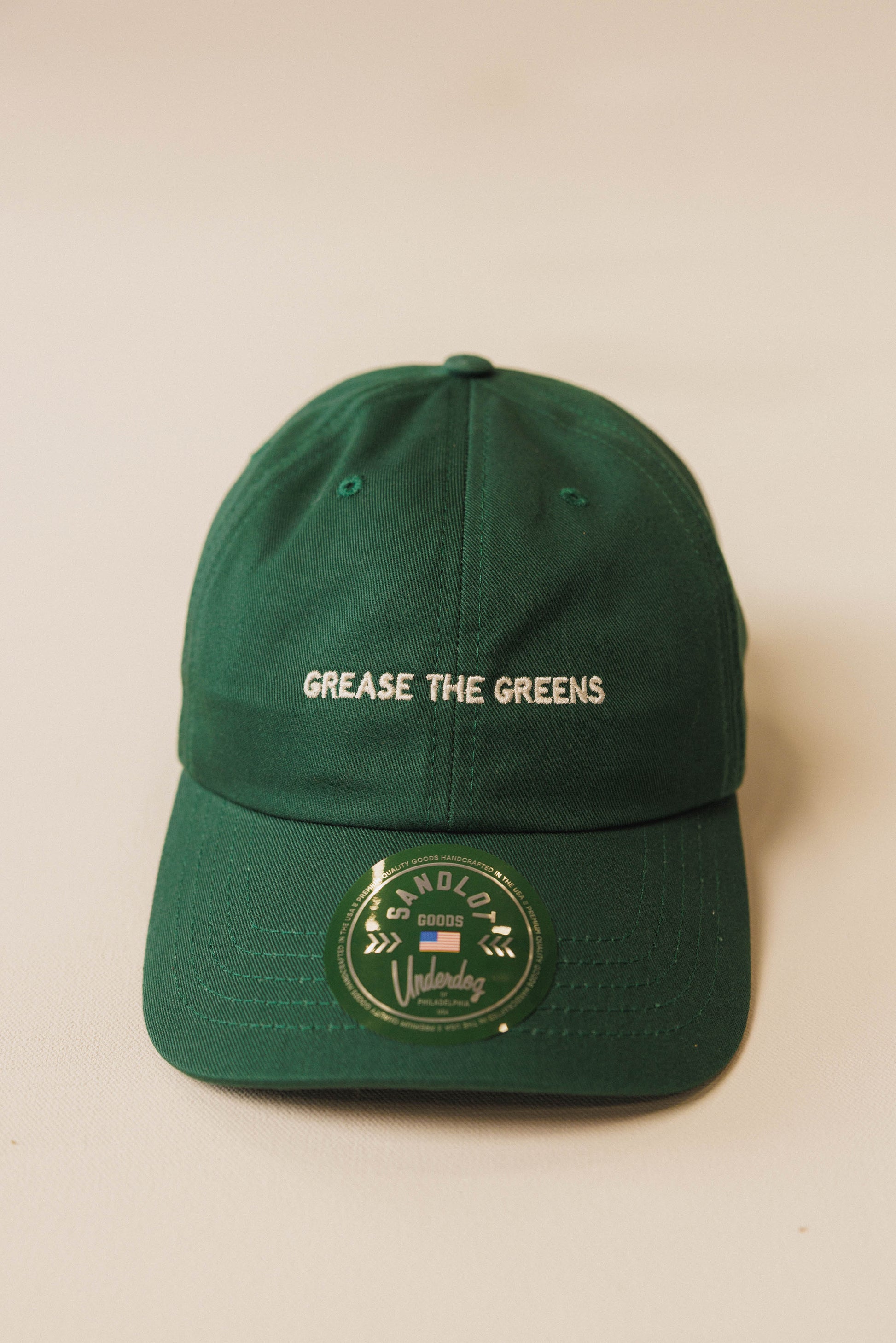 Green cap with 'Grease the Greens' text on a beige background