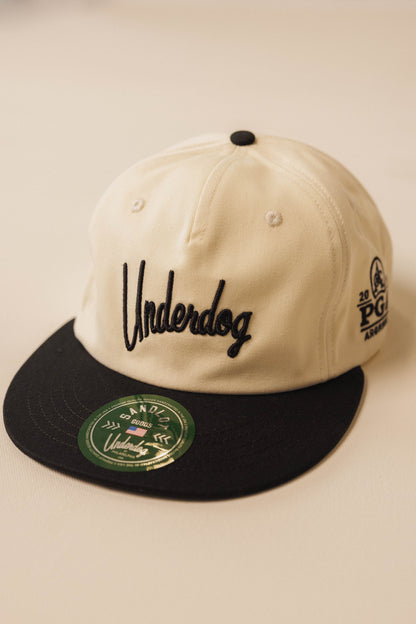 Two-tone cap with 'Underdog' branding on a beige background