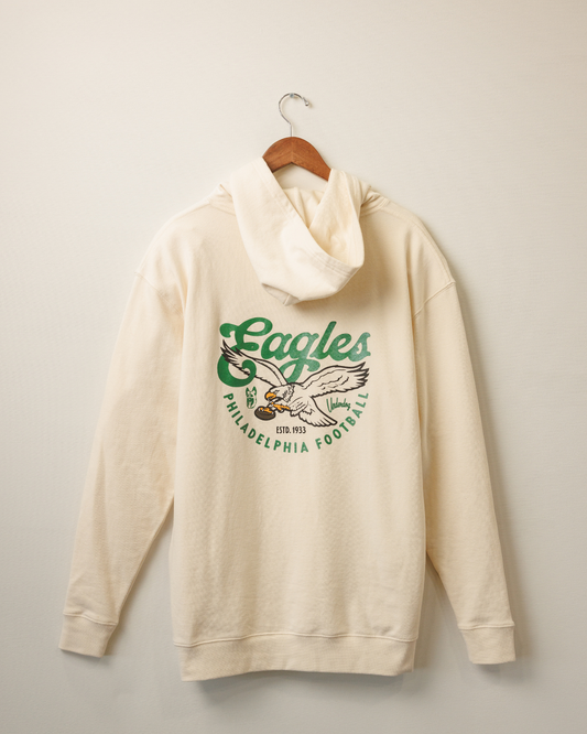 Beige hoodie with Eagles logo on a hanger against a beige wall