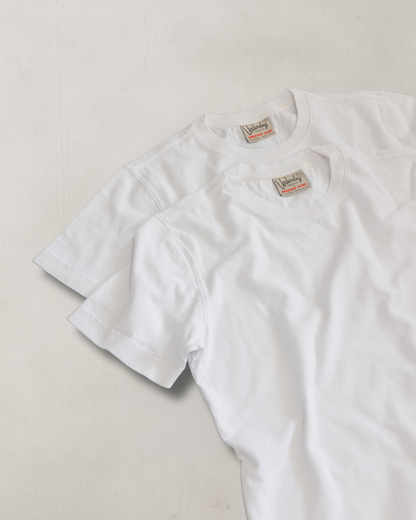 Two white t-shirts with labels on a light gray background
