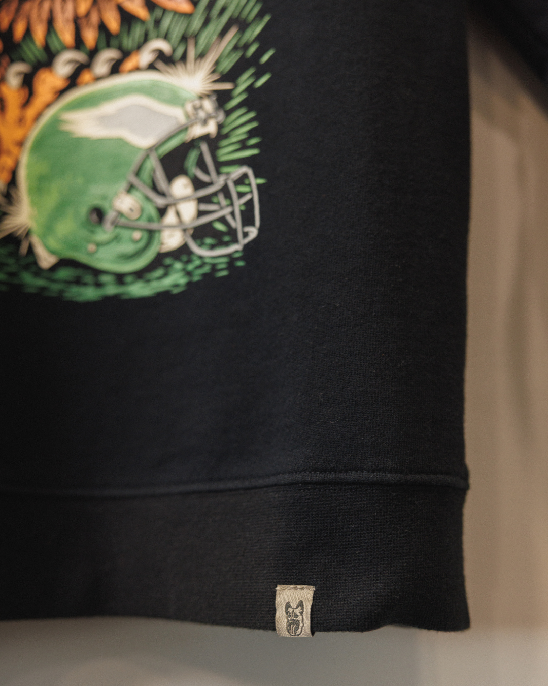 Black sweatshirt with a colorful graphic design on the sleeve, featuring a football helmet and leaves.