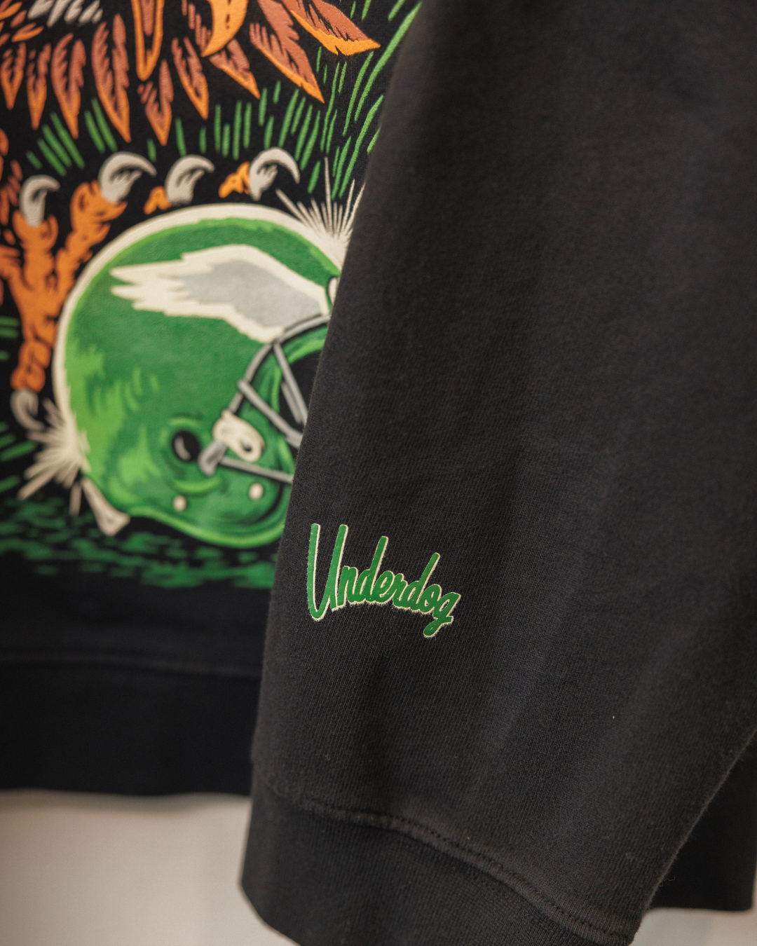 Black sweatshirt with 'Underdog' logo and colorful graphic design in the background