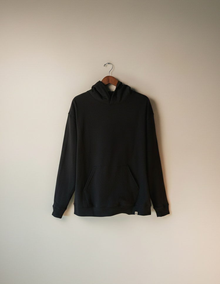 Black hoodie on a wooden hanger against a beige wall