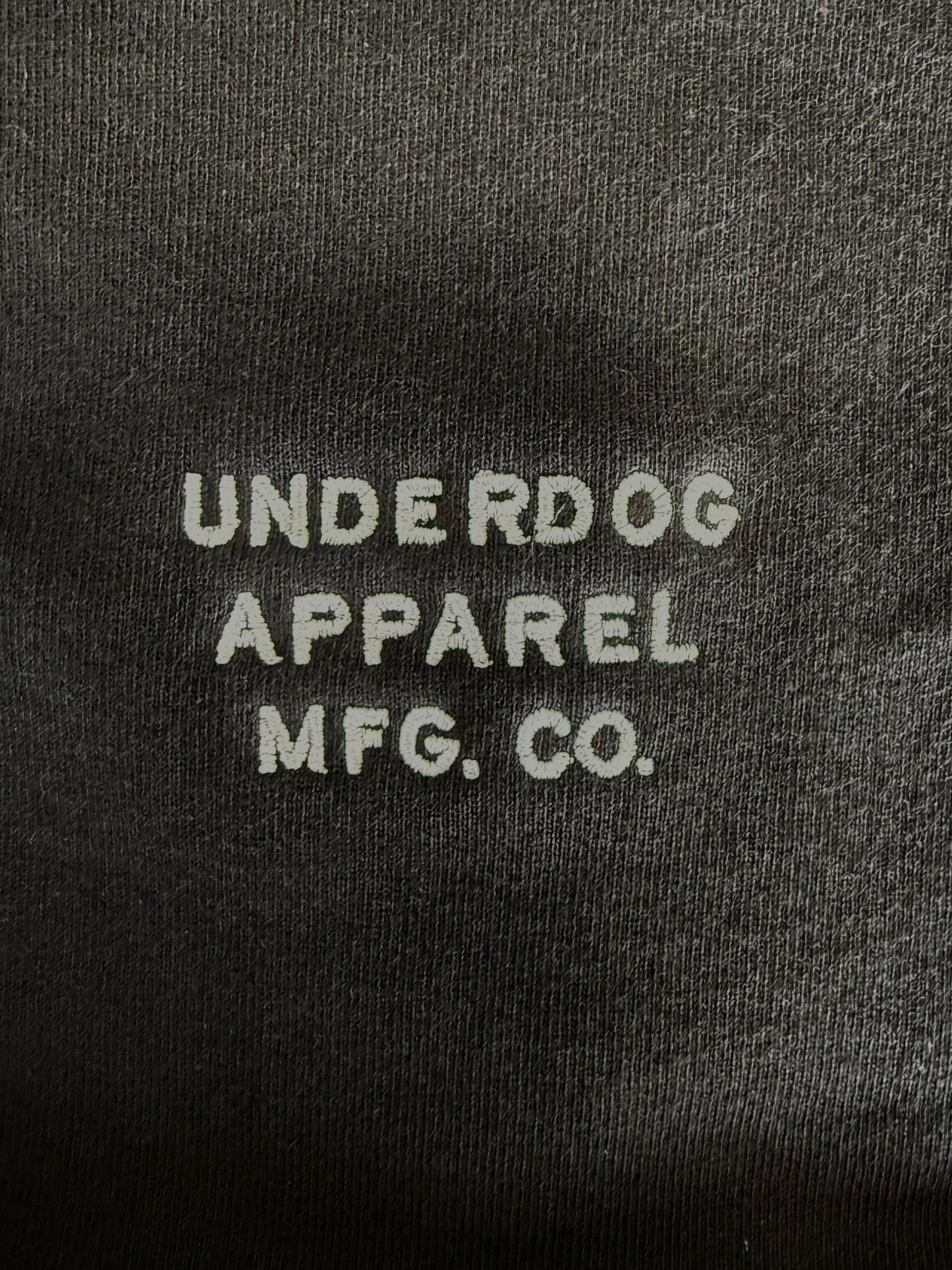Embroidered text 'UNDERDOG APPAREL MFG. CO.' on a dark fabric background