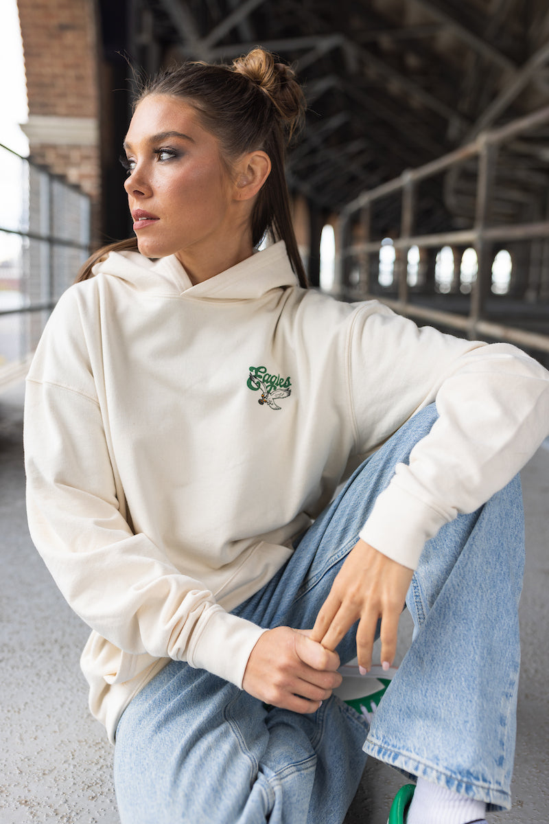 Person wearing a white hoodie with a logo and blue jeans sitting on a concrete surface.