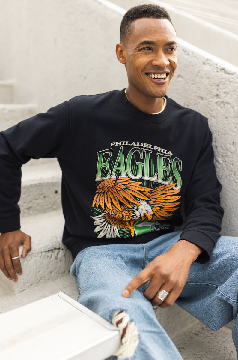Man wearing a black Philadelphia Eagles sweatshirt sitting on steps.