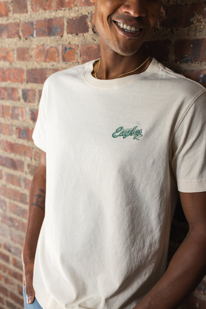 Person wearing a white t-shirt with a logo against a brick wall