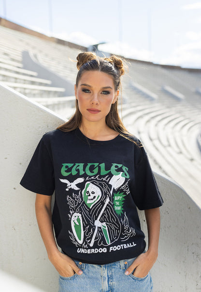 Woman wearing a black t-shirt with graphic design and text, standing against a white architectural background.