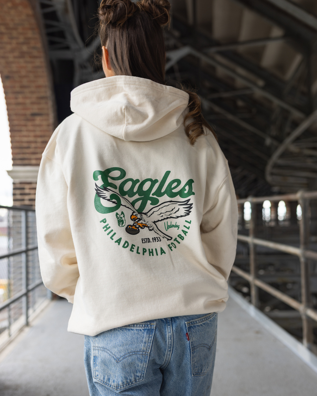 Person wearing a cream hoodie with 'Eagles' logo on the back, standing on a bridge.