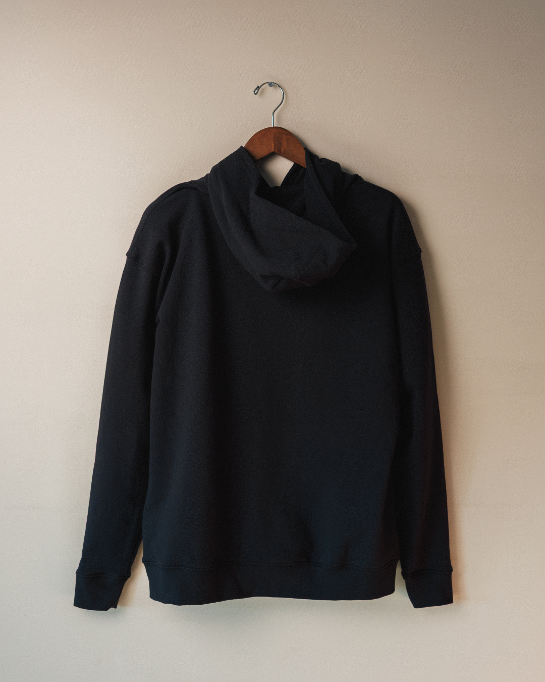 Navy hoodie on a hanger against a beige wall