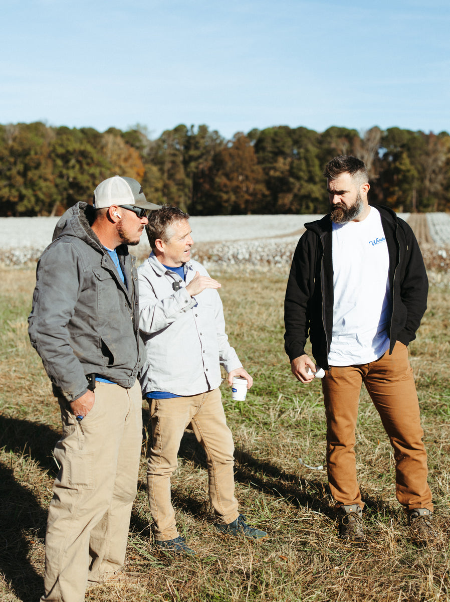 Three people standing in a field with trees in the background